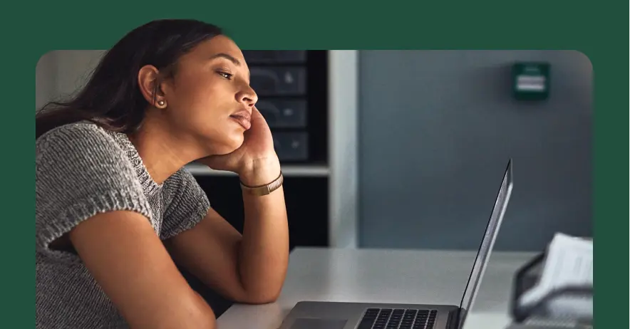 A woman sitting at a desk and looking unengaged at her laptop screen.