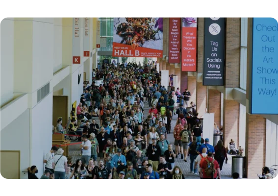 A large crowd of people walking through a convention hall at Gen Con.
