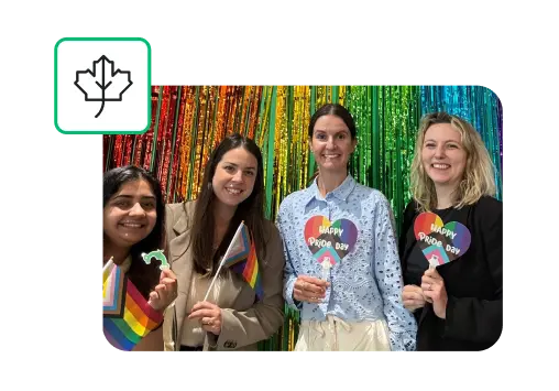 Four smiling women holding Happy Pride Day signs and flags, next to leaf icon