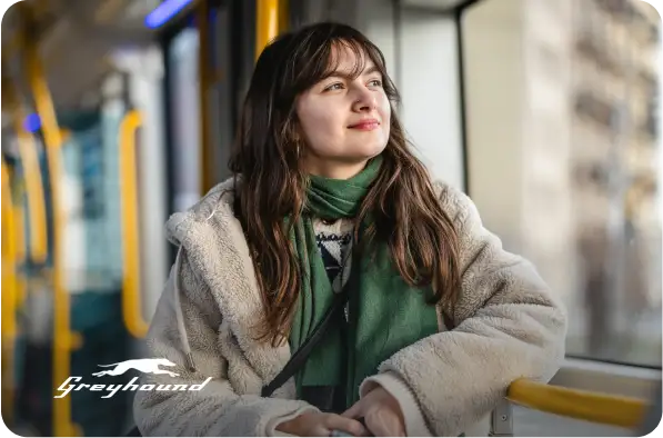 Woman looking out a window of a bus with Greyhound logo