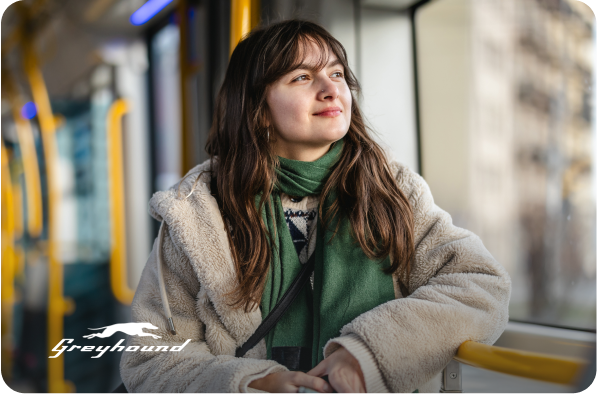woman looking out a window of a bus with greyhound logo