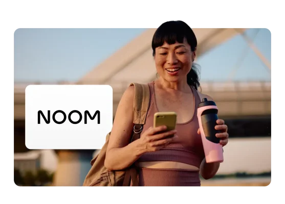 Noom app user smiling at her phone during an outdoor workout, with the Noom logo