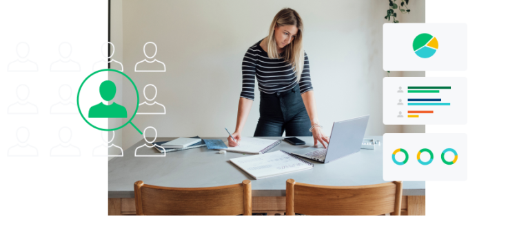 Woman standing over a table while looking at a laptop screen and writing on a notebook