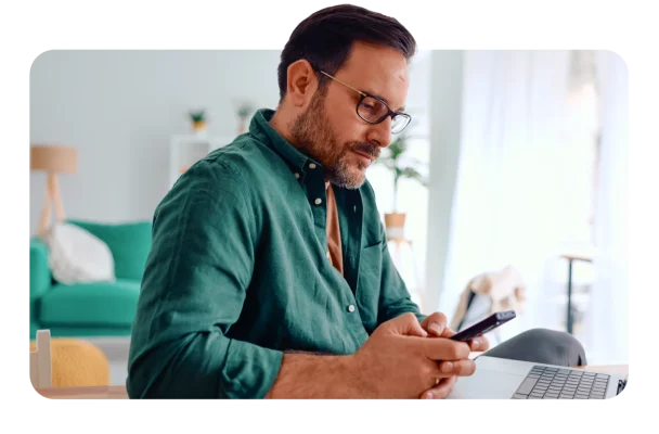 Man typing on phone with an open laptop