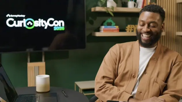 Smiling man sitting, with CuriosityCon logo in the background