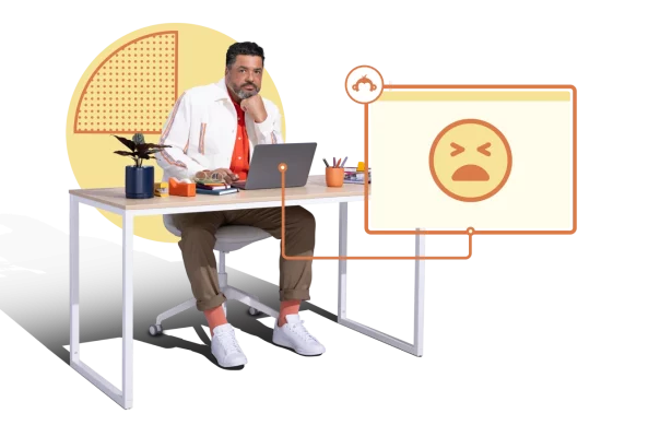 Frowning man sitting at desk with laptop open, with sad emoji next to him