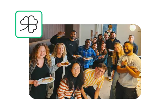 A group of SurveyMonkey employees smiling and holding plates of food, next to an icon of a three leaf clover
