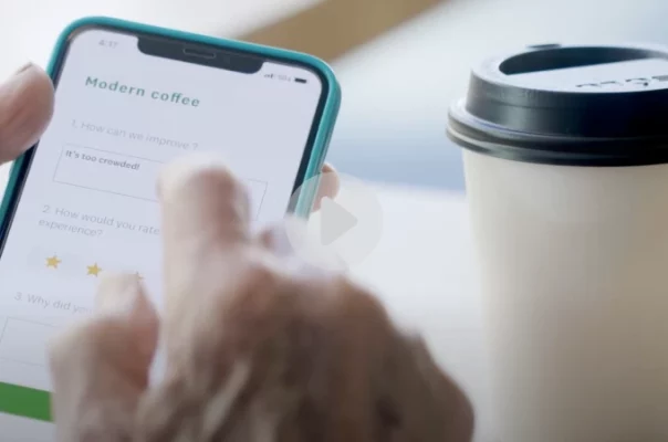 Hands holding a phone with a SurveyMonkey survey on it, next to a coffee cup