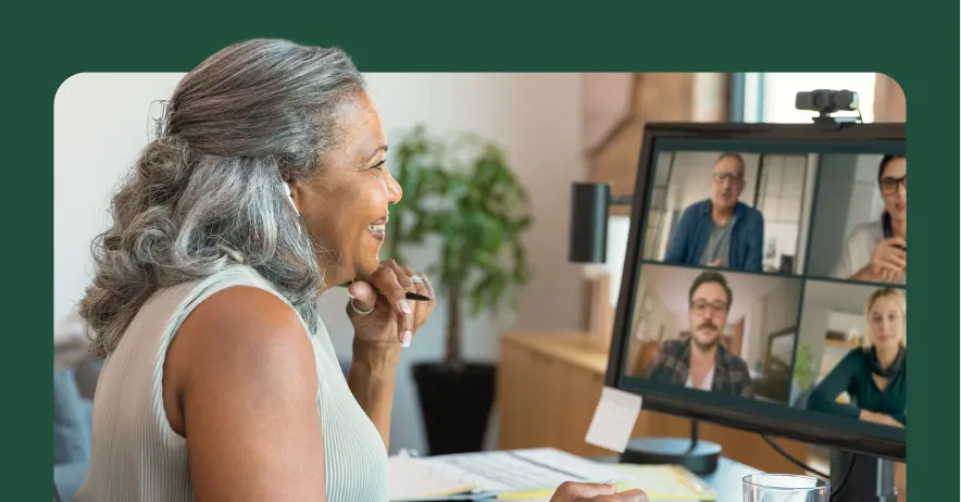 A woman smiling during a video conference call with four participants on her monitor.