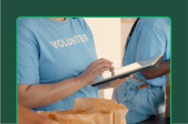 Trabalhadora voluntária digitando em um tablet ao lado de sacolas de papel.