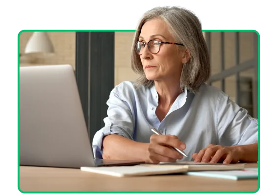 Woman looking at a laptop screen and writing on a notepad