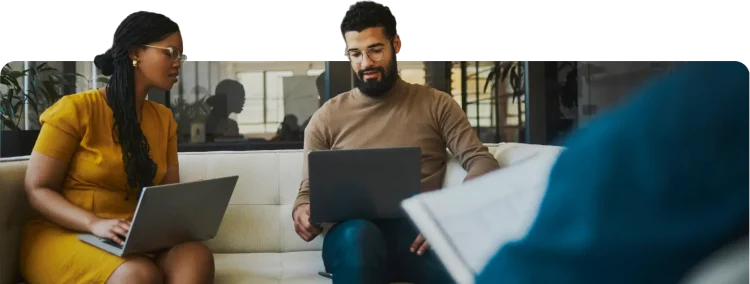 Professional team collaborating on laptops on a sofa in a modern office environment.