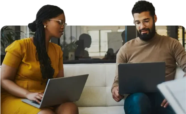 Professional team collaborating on laptops on a sofa in a modern office environment.