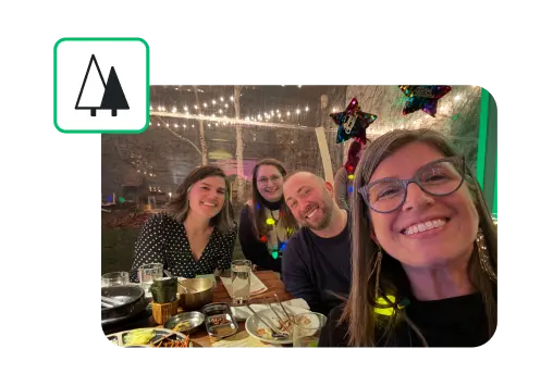 A group of smiling SurveyMonkey employees standing around a table with food, next to an icon of trees