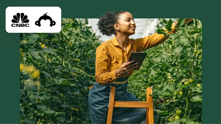 A small business owner in a greenhouse checking crops with a tablet, featuring the CNBC and SurveyMonkey logos.