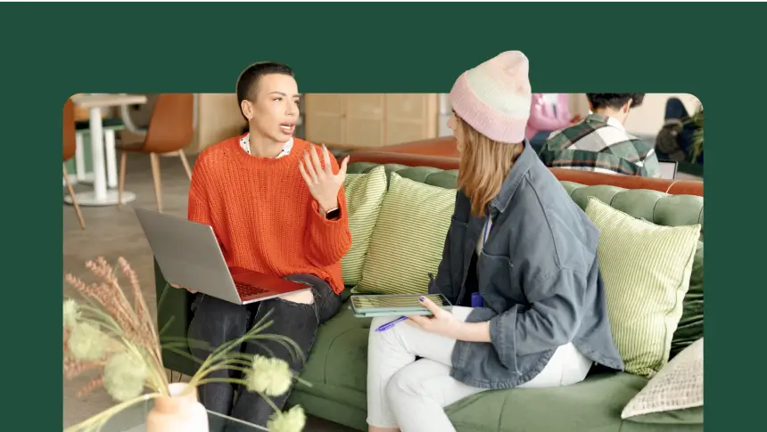 Duas pessoas sentadas em um sofá conversando e olhando para um laptop.