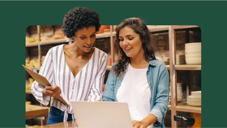two women standing up collaborating on a laptop in a warehouse