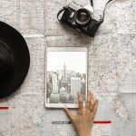 Encuesta para viajes: tablet que muestra la foto de una ciudad, cámara y sombrero sobre un mapa