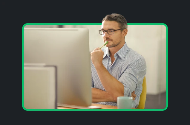 man at computer holding pen and thinking