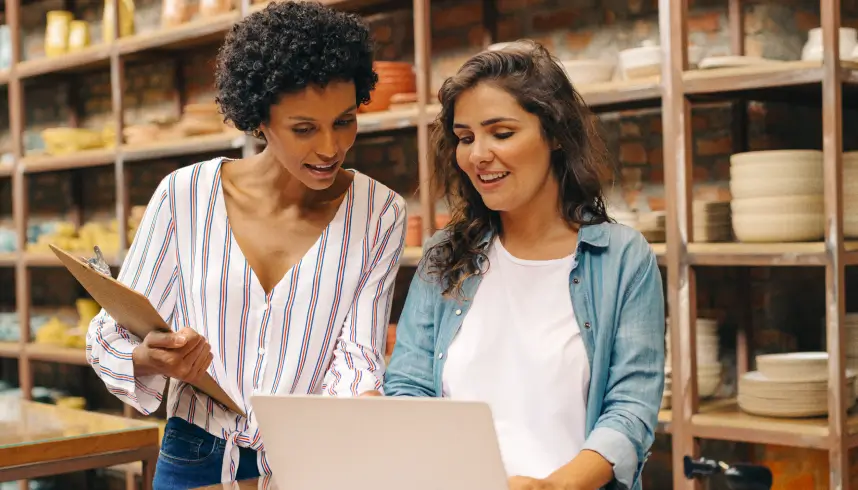 Two women standing up collaborating on a laptop in a warehouse