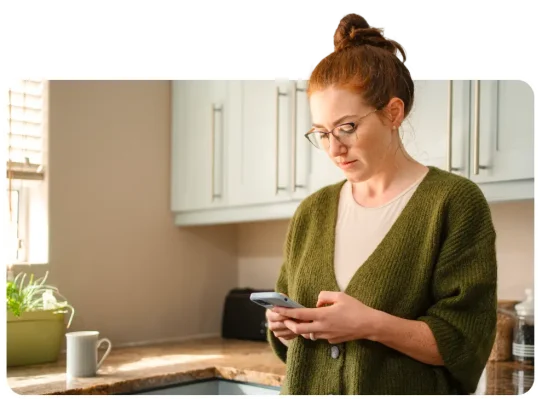 Kvinne som står på kjøkkenet og skriver på telefonen
